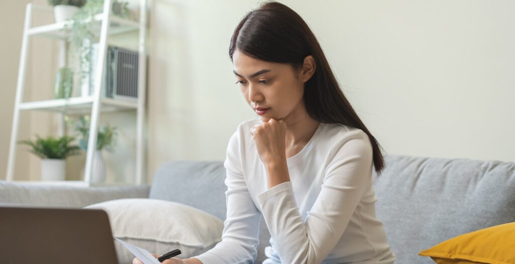 Person Reviewing Paperwork on Couch with Laptop